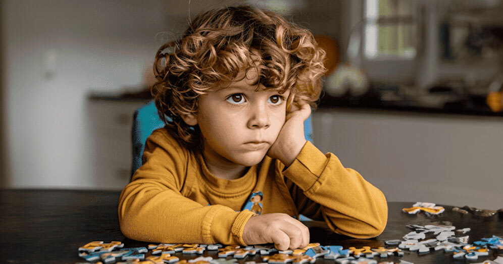Child contemplating puzzle pieces on a table, symbolizing the thoughtful approach needed in therapy.